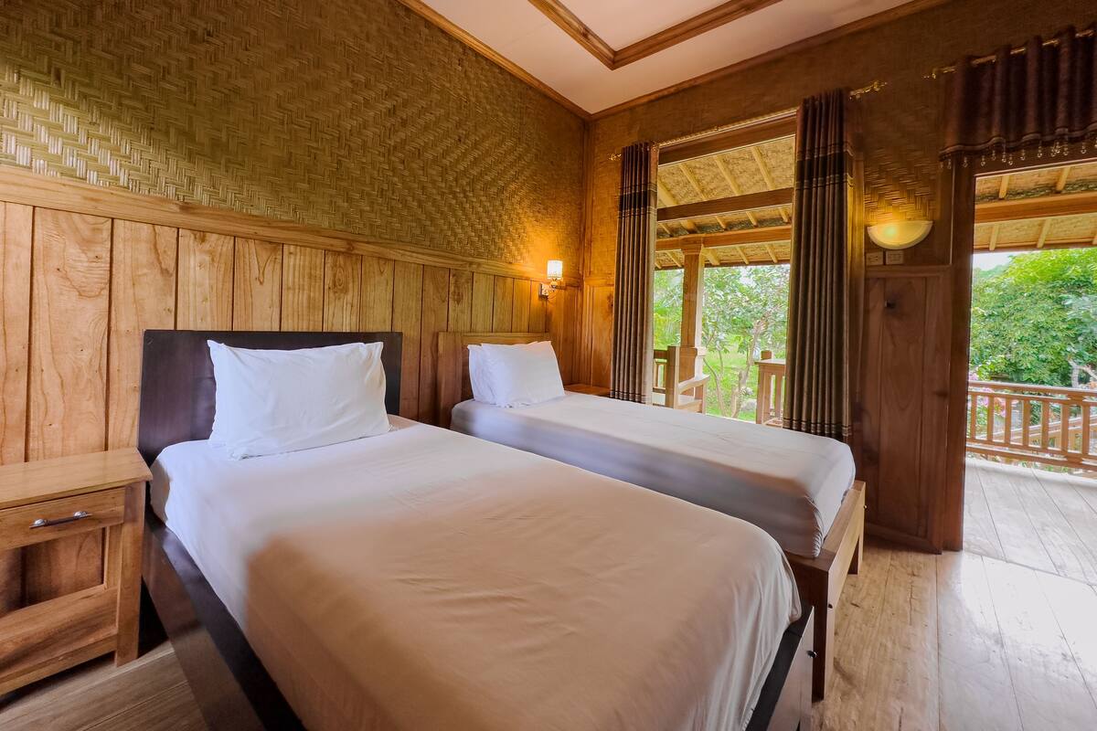 Ein Zimmer mit zwei Betten, Holzwänden, einem Balkon mit Blick ins Grüne und einer Holzbalkendecke.