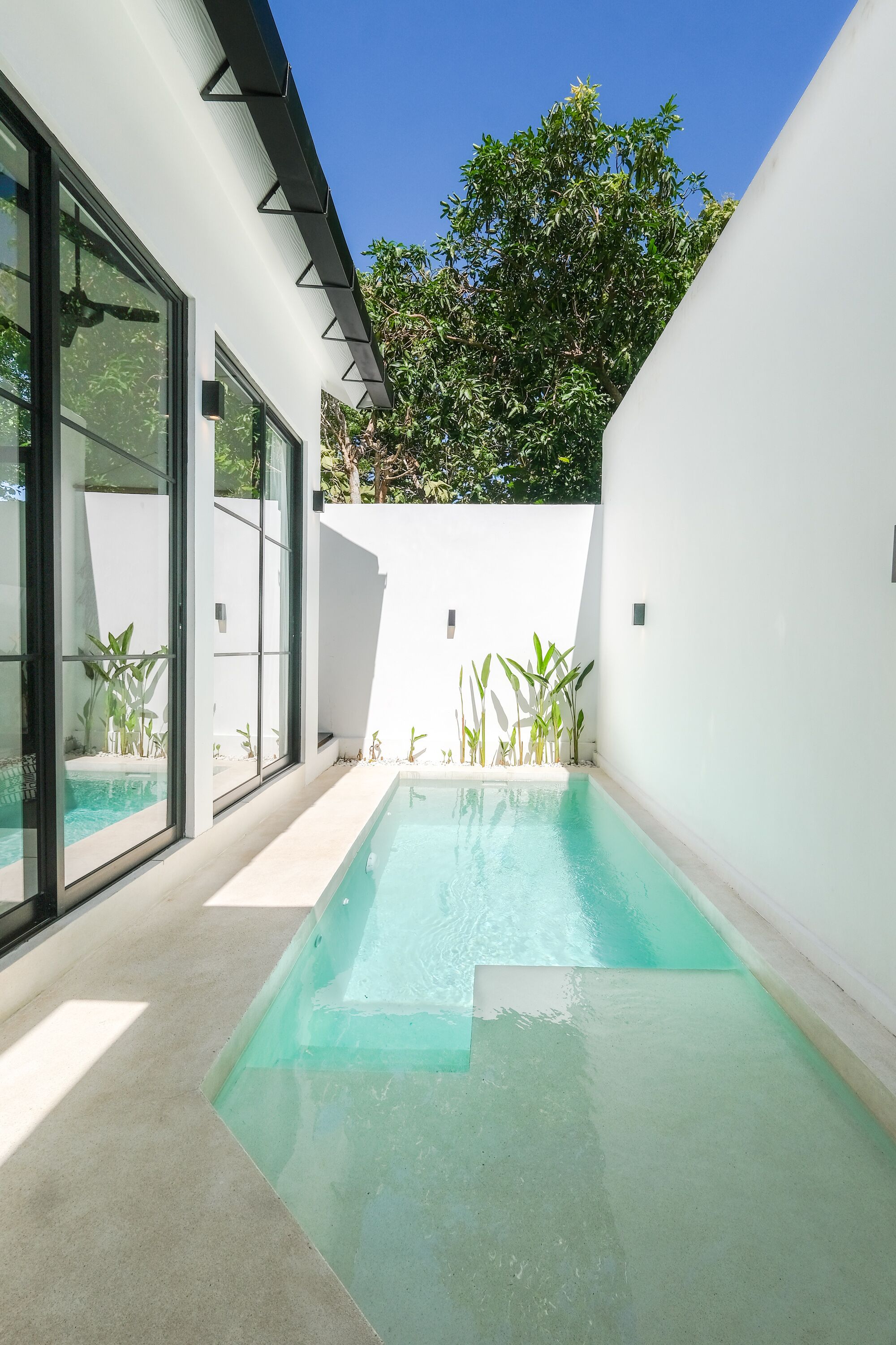 Et moderne poolområde med glasvægge, en betonflisebelagt terrasse og en hvid væg med et trekantet design.