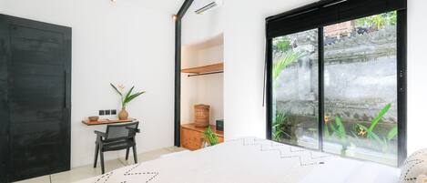 Een moderne slaapkamer met een bed, een bureau en uitzicht op een tuin door een schuifdeur.