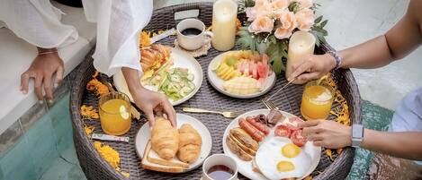 A wicker table with breakfast items, including croissants, eggs, and fruit, surrounded by candles and flowers.