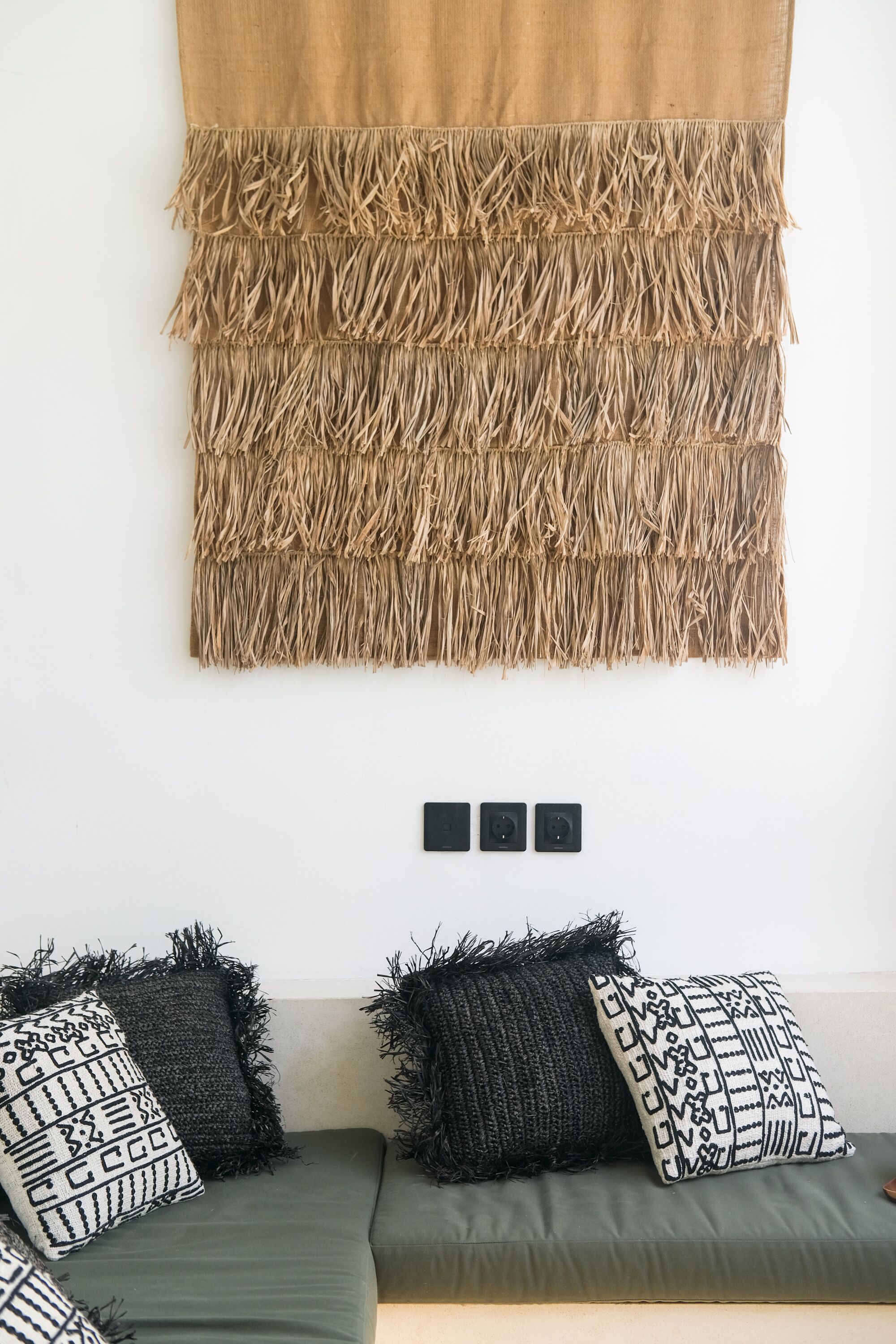 A room with a green sofa, black and white patterned pillows, and a woven tapestry on the wall.