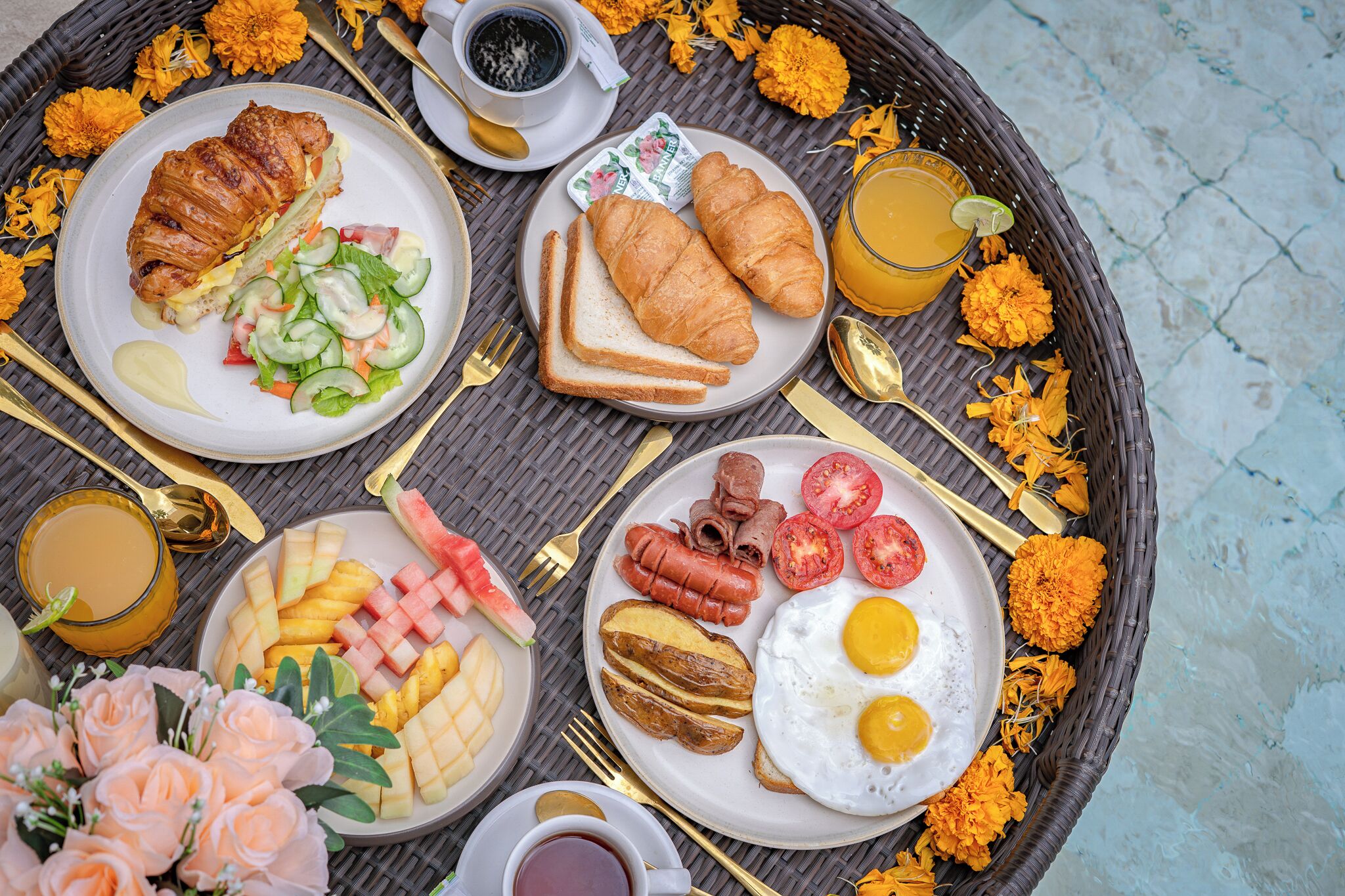A breakfast tray with croissants, eggs, sausages, and fruit.