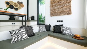 Ein modernes Wohnzimmer mit einem grünen Sofa, gemusterten Kissen, Wandkunst aus gewebtem Material und einer Holzschüssel auf einem Beistelltisch.