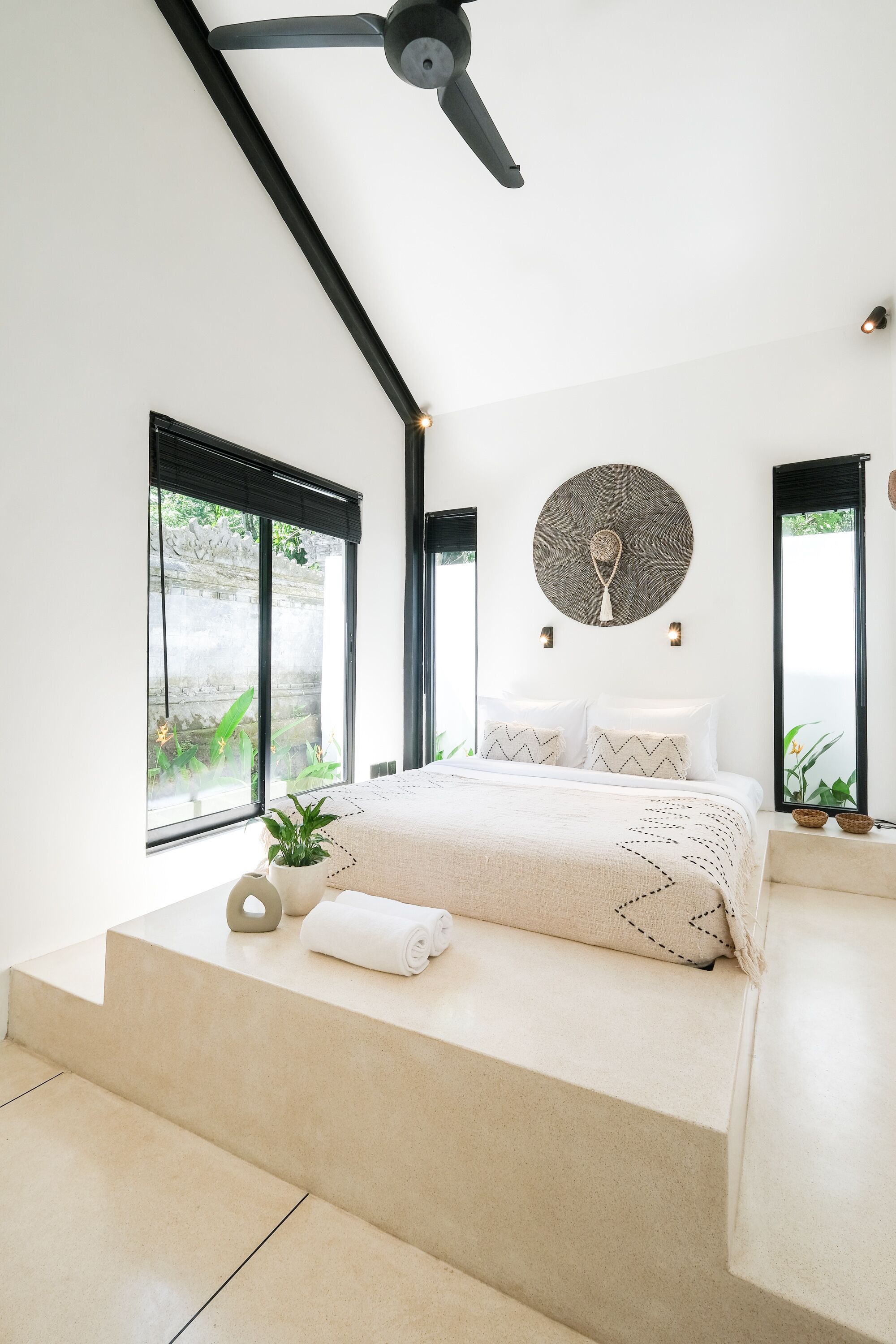 Ein modernes Schlafzimmer mit Bett, Deckenventilator und großen Fenstern.