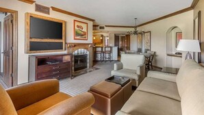 Un salon spacieux avec une cheminée, des sièges confortables, un téléviseur et, au fond, un coin repas.