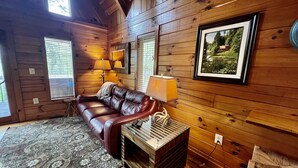 A cozy cabin interior with a leather sofa, a patterned rug, wooden walls, and a framed picture on the wall. - New Hot Tub & Trailer Parking @ Cliff Eagle (Stanton)