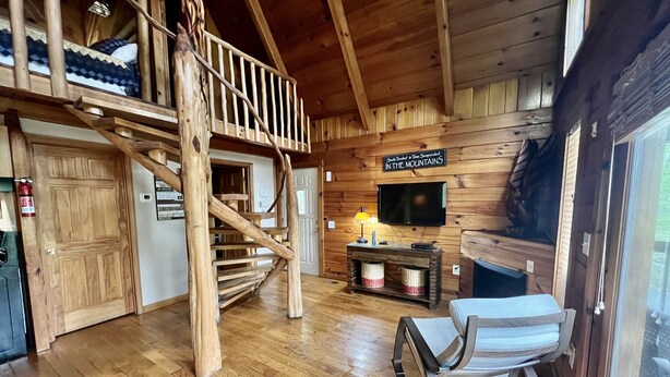 A rustic cabin interior with a wooden staircase, a television mounted on the wall, and a fireplace. - New Hot Tub & Trailer Parking @ Cliff Eagle (Stanton)