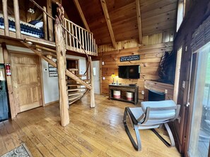 Een landelijk chalet interieur met een houten trap, een aan de muur bevestigde televisie en een open haard.
