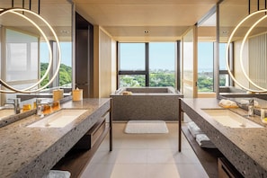A modern bathroom with two sinks, large mirrors, and a view of a cityscape through large windows.