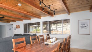 Un coin repas avec une table et des chaises en bois, un canapé gris et une fenêtre avec des stores.