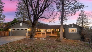 A two-story house with a garage, a covered deck, and a large tree in front. - 8BR Yosemite Escape w/ Views & Spa - Game Room & Pet-Friendly (Oakhurst)