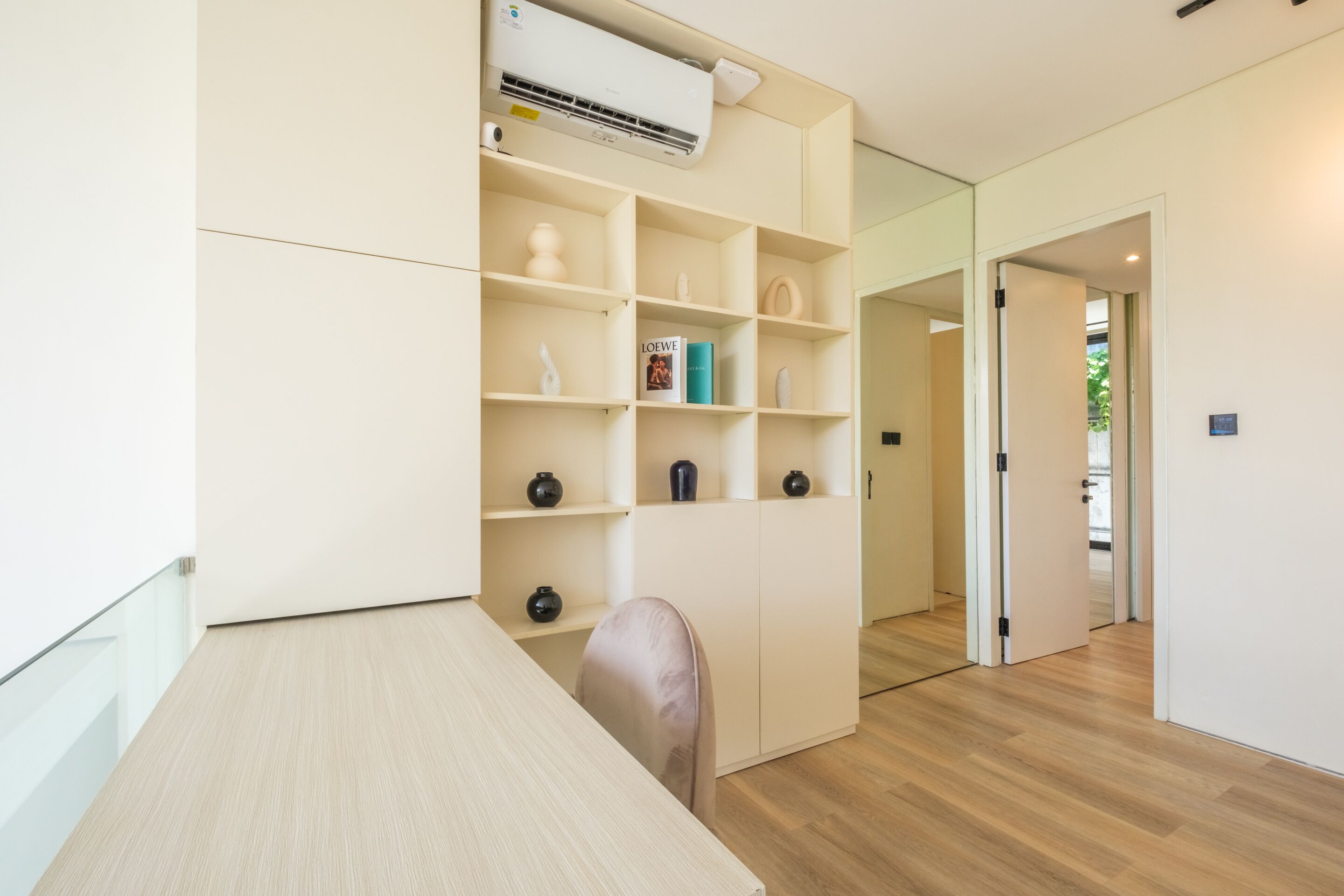 A modern room with a wooden floor, a white desk, a chair, and a built-in shelving unit with decorative items.