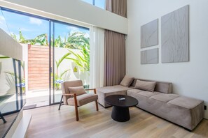 Un salon moderne avec un canapé beige, une table basse ronde et une porte en verre donnant sur un balcon agrémenté de plantes.