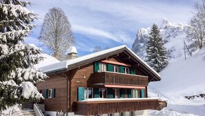 Un chalet en bois doté d’un balcon, entouré d’arbres et de montagnes couverts de neige.