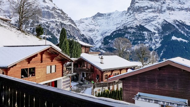 Un chalet de montagne avec des cabanes en bois, un télésiège et, en arrière-plan, des montagnes enneigées.