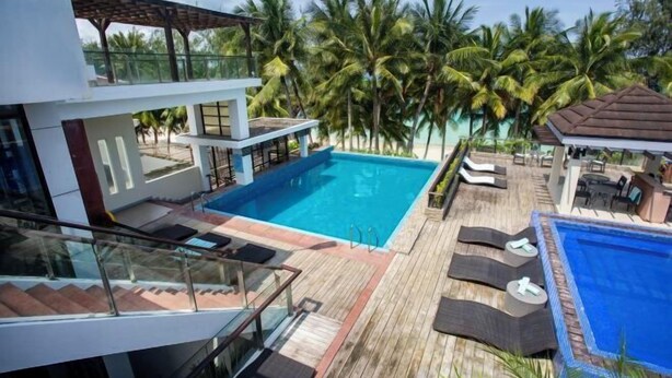 A modern resort with a large swimming pool, lounge areas, and a view of palm trees. - Crown Regency Beach Resort (Boracay Island)