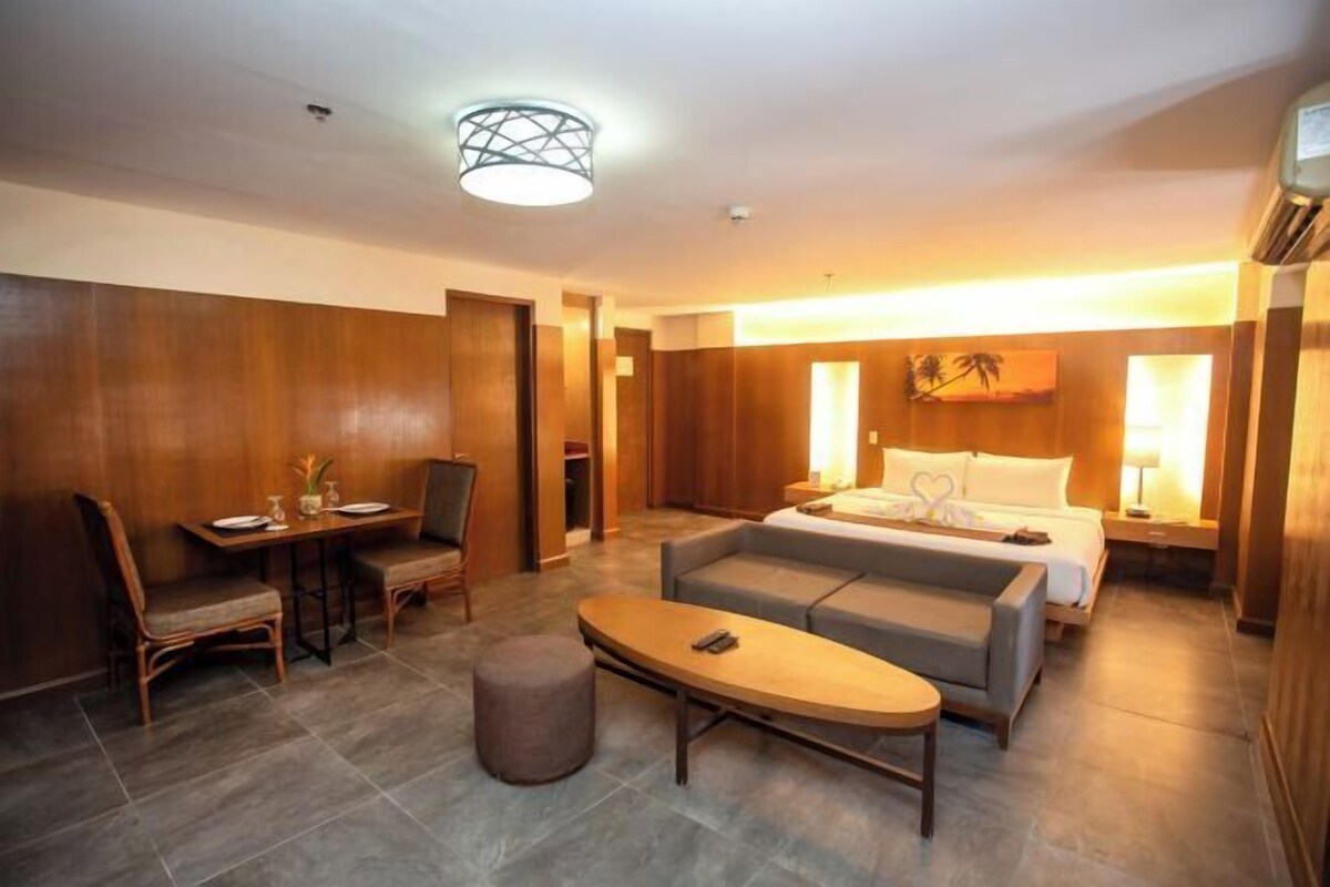 A hotel room with a bed, a sofa, a dining table with chairs, and a small round table.