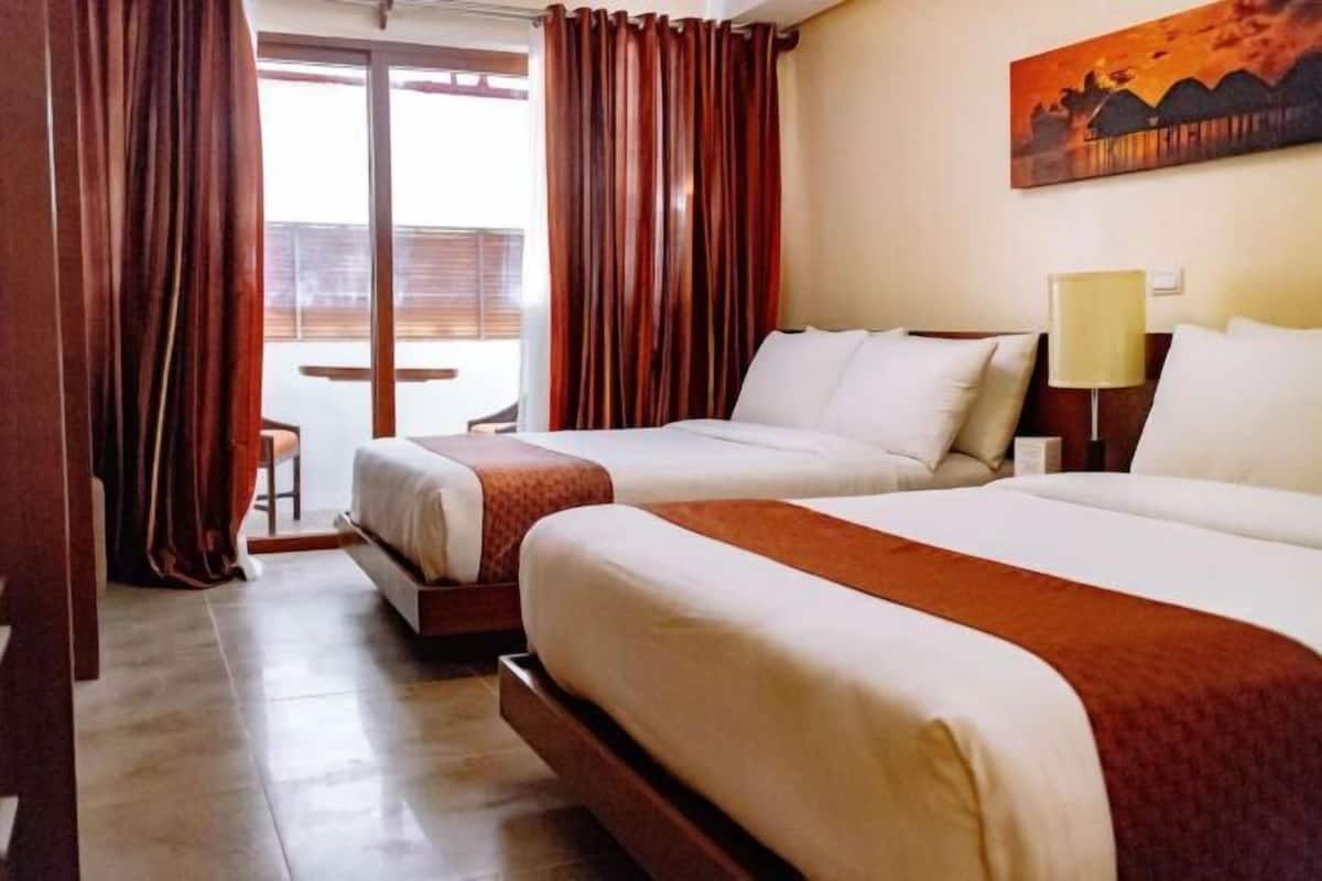 A hotel room with two beds, a large window with curtains, a painting on the wall, and a lamp on the nightstand.