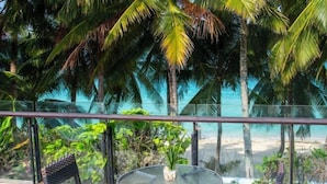 A balcony with a glass railing, a round table, two wicker chairs, and a view of the beach and palm trees. - Crown Regency Beach Resort (Boracay Island)