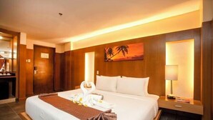 A hotel room with a large bed, a wooden headboard, a painting of palm trees, a nightstand with a lamp, and a view of the outside. - Crown Regency Beach Resort (Boracay Island)