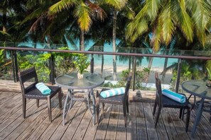 A wooden deck with a glass balustrade, two wicker chairs with blue cushions, and a round glass table. - Crown Regency Beach Resort (Boracay Island)