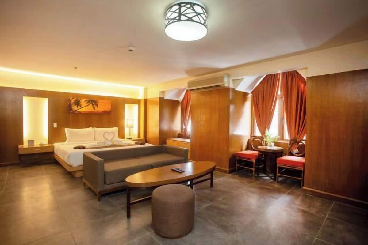 A hotel room with a bed, sofa, coffee table, and a small dining area.