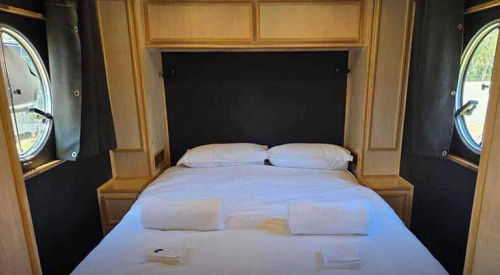 Una cama con sábanas y almohadas blancas, un cabecero de madera y dos mesitas de noche.