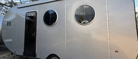 Un remolque estacionario con una puerta, dos ventanas redondas y un escalón que lleva a la entrada.
