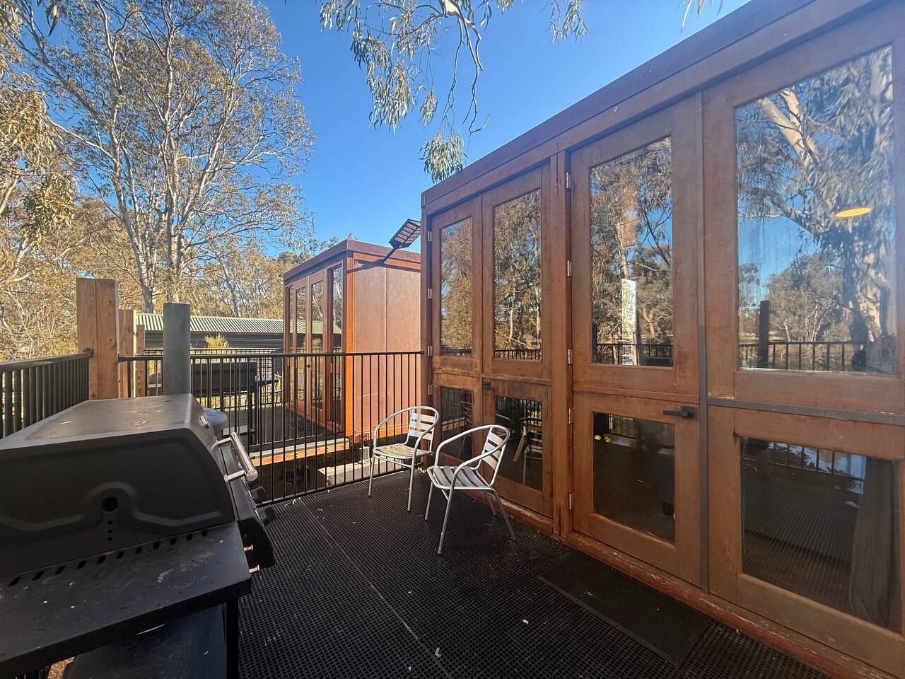 A covered outdoor patio with a grill, two chairs, and a wooden deck.