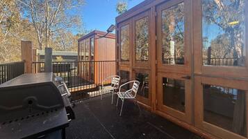 A covered outdoor patio with a grill, two chairs, and a wooden deck.