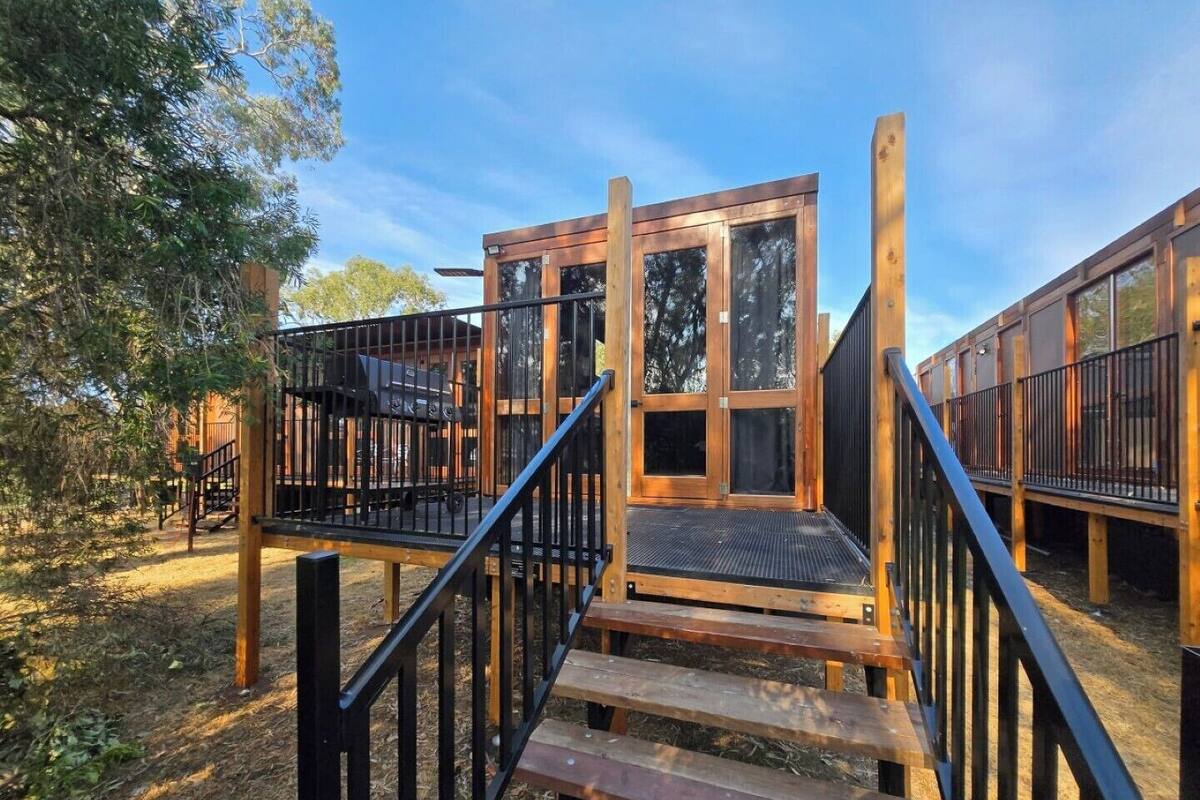 Una terraza de madera con una escalera que conduce a una plataforma elevada, rodeada de árboles.