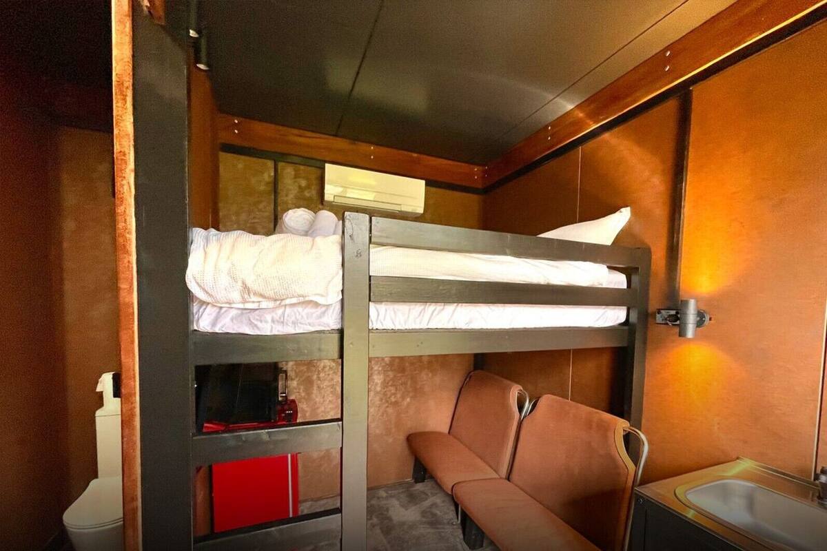 Una cama litera con un almacenamiento rojo debajo, un banco, un lavamanos y un espejo.