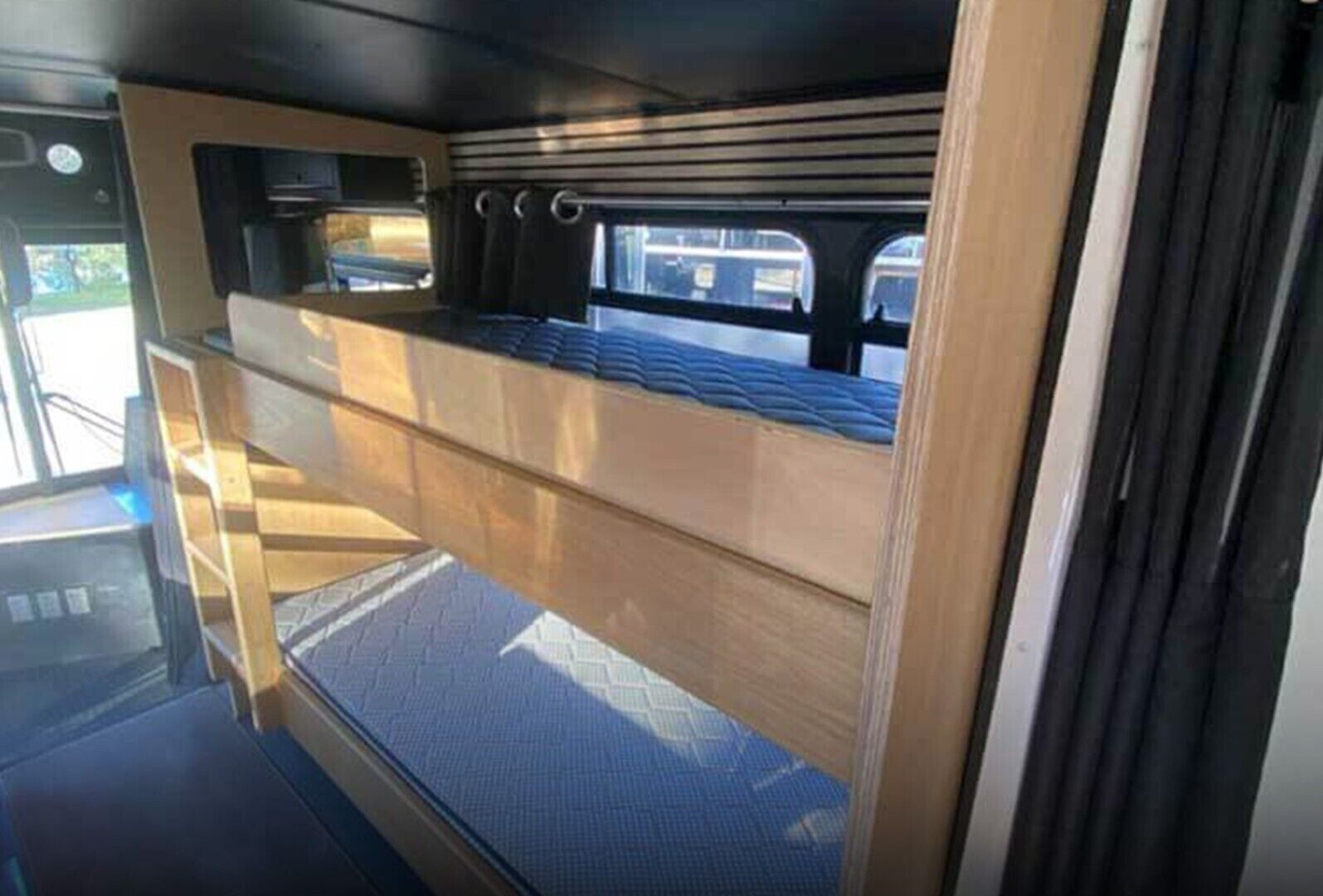 Ein kompaktes Wohnmobil-Interieur mit Etagenbett, kleiner Küchenzeile und einem Fenster mit Ausblick nach draußen.