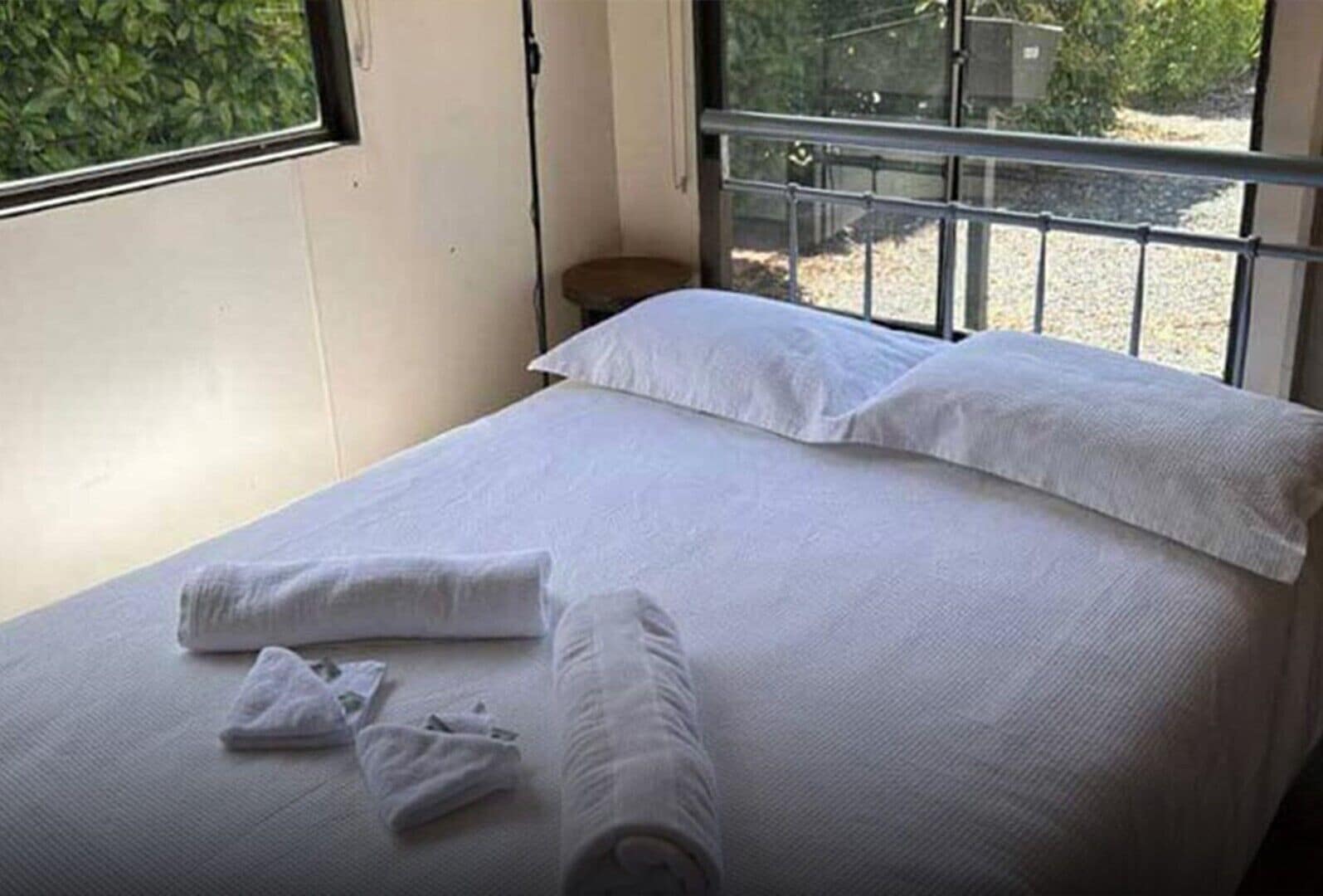 Un letto ben rifatto con lenzuola e cuscini bianchi, un comodino e una finestra con vista sul verde.