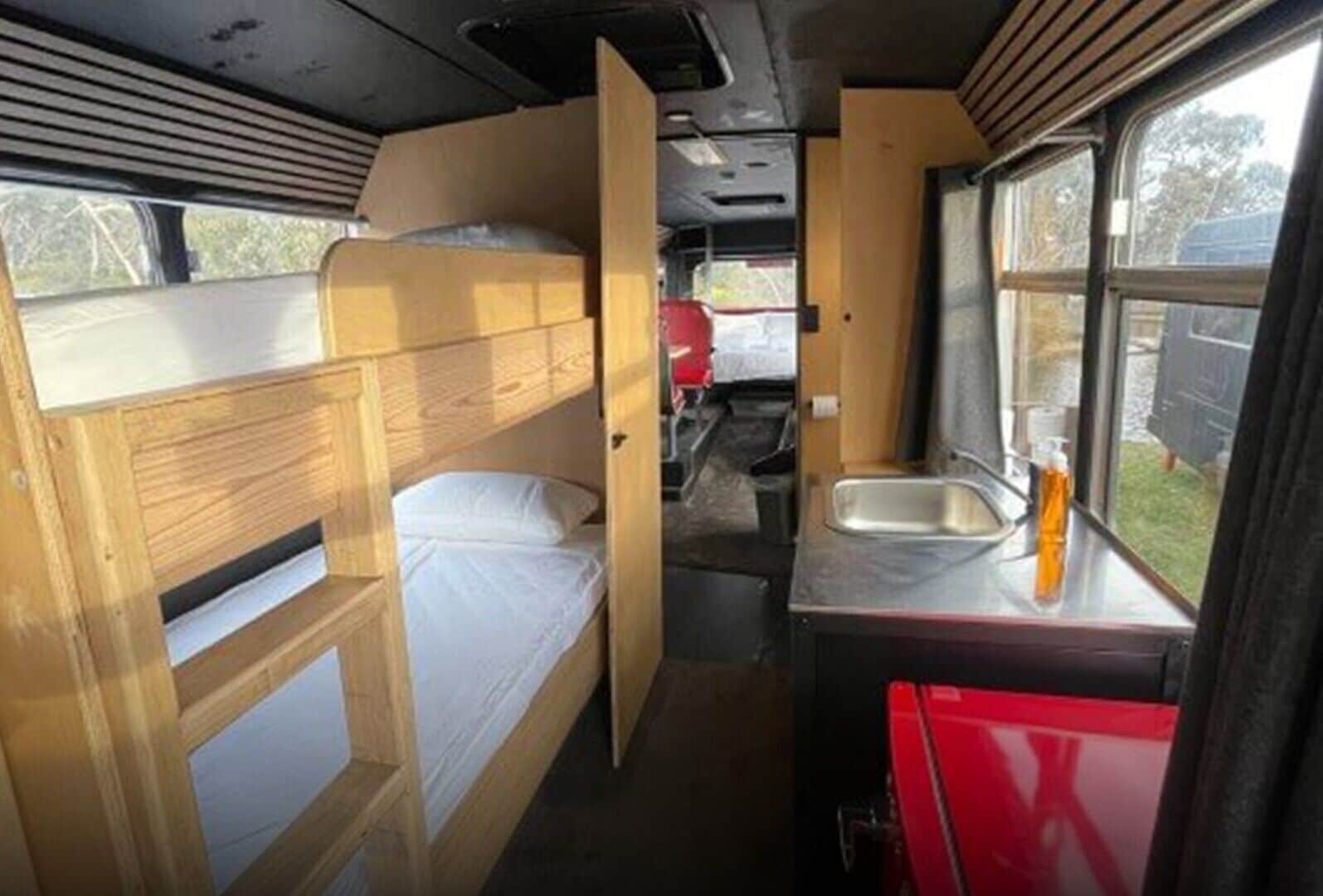 A compact RV interior with a bunk bed, a kitchenette with a sink, and a window providing a view of the outside.