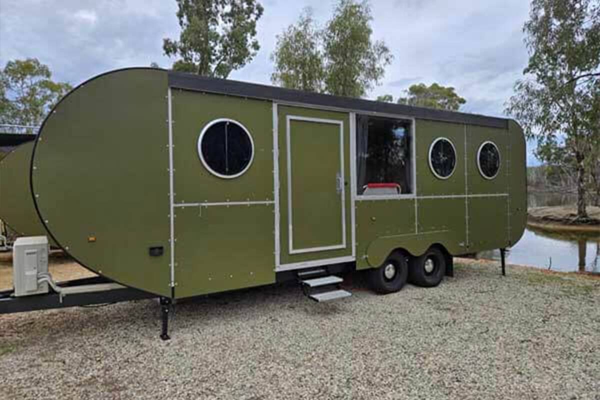 Una caravana verde con una puerta, dos ventanas y un escalón que lleva a la entrada.