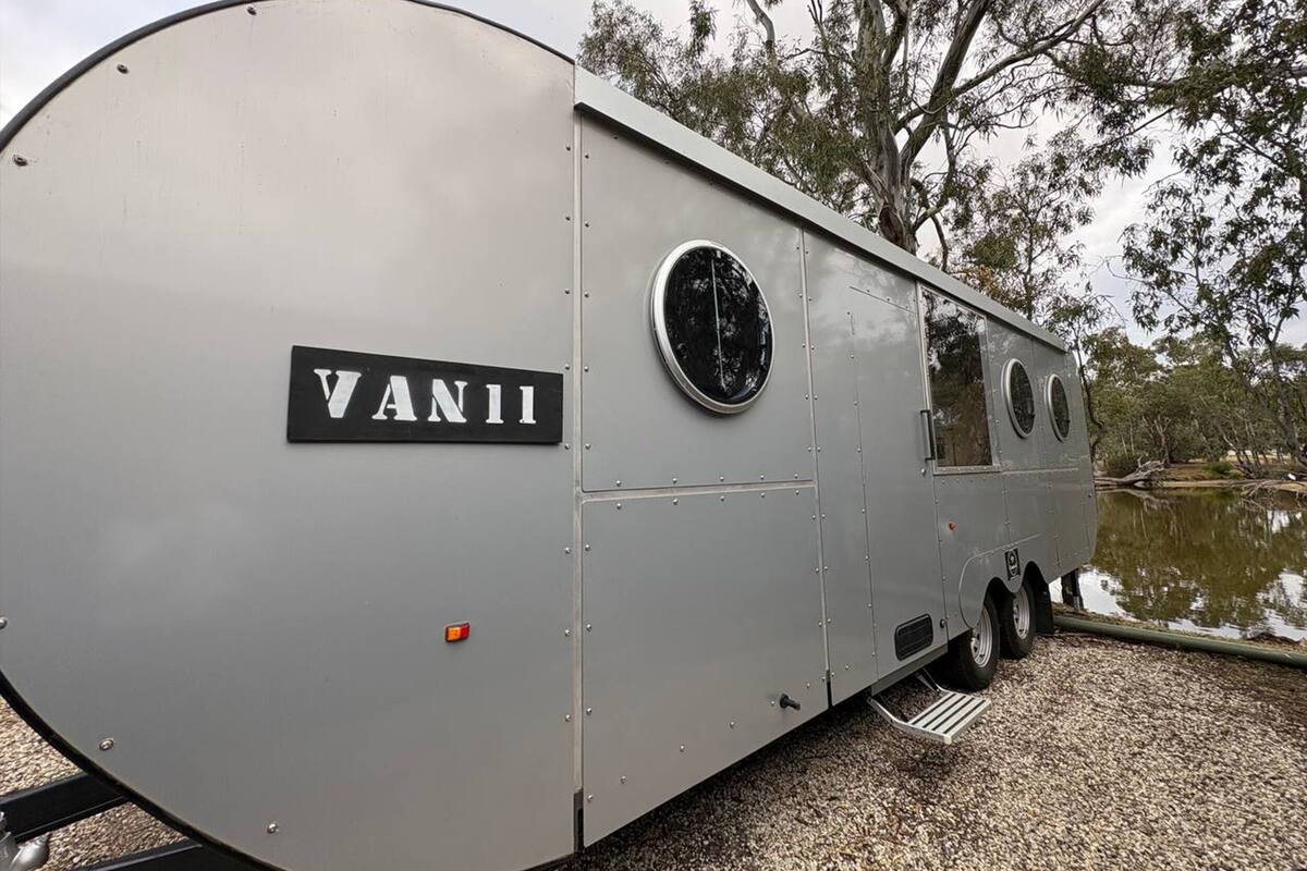 Una caravana gris con el nombre 'VAN11' en la carrocería, una ventana circular y una puerta pequeña.