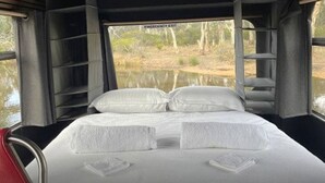 A bed with white linens and pillows, a red chair, and a window with a view of a water body and trees. - Stawell Grampians Gate C & C Park (Stawell)