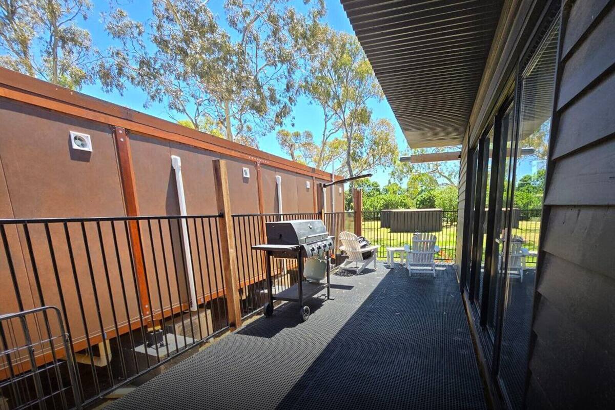 Un patio cubierto con una parrilla, mobiliario exterior y vistas al jardín trasero.