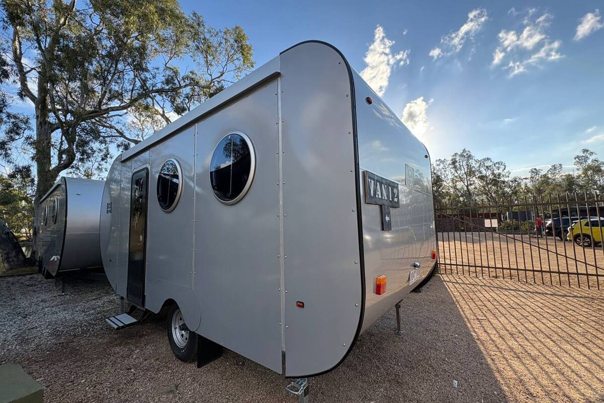Una caravana plateada con el rótulo 'VAN12', una ventana circular y una puerta.