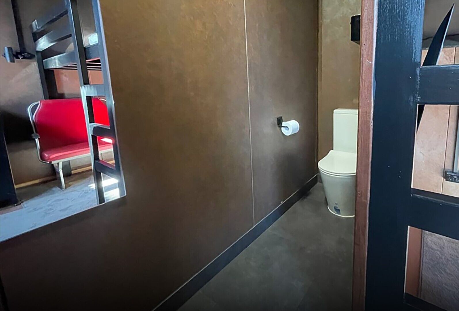 A bathroom with a toilet, a red chair, and a wooden door.