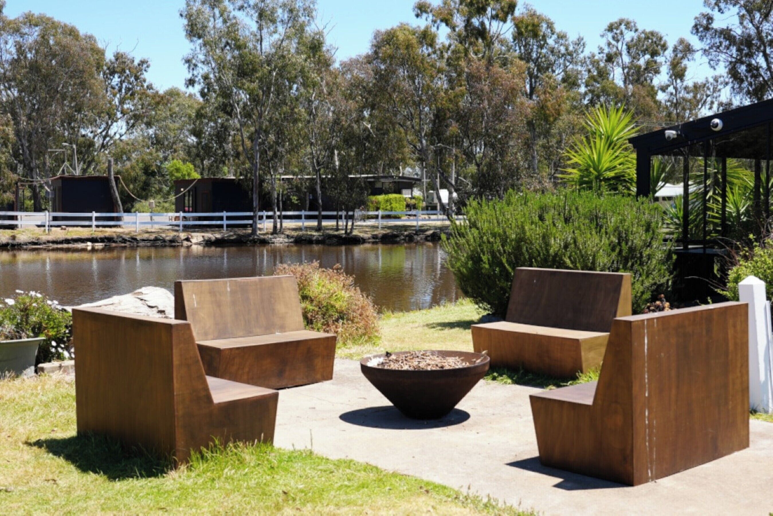 Outdoor seating with a fire pit, a body of water, and trees in the background.