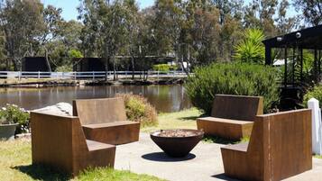 Outdoor seating with a fire pit, a body of water, and trees in the background.