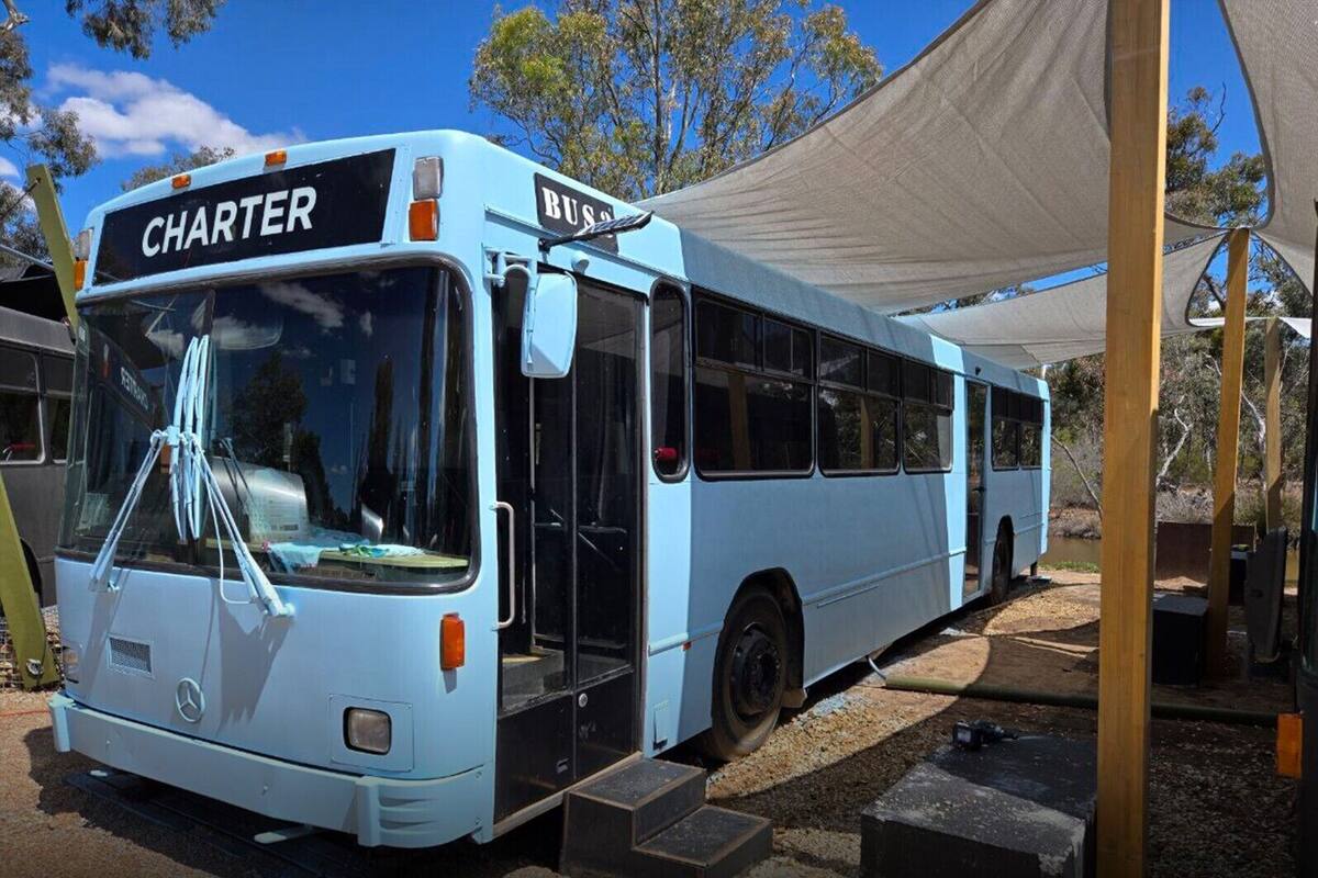 Un autobús azul claro con la palabra 'CHARTER' escrita en la parte delantera, estacionado bajo un toldo.