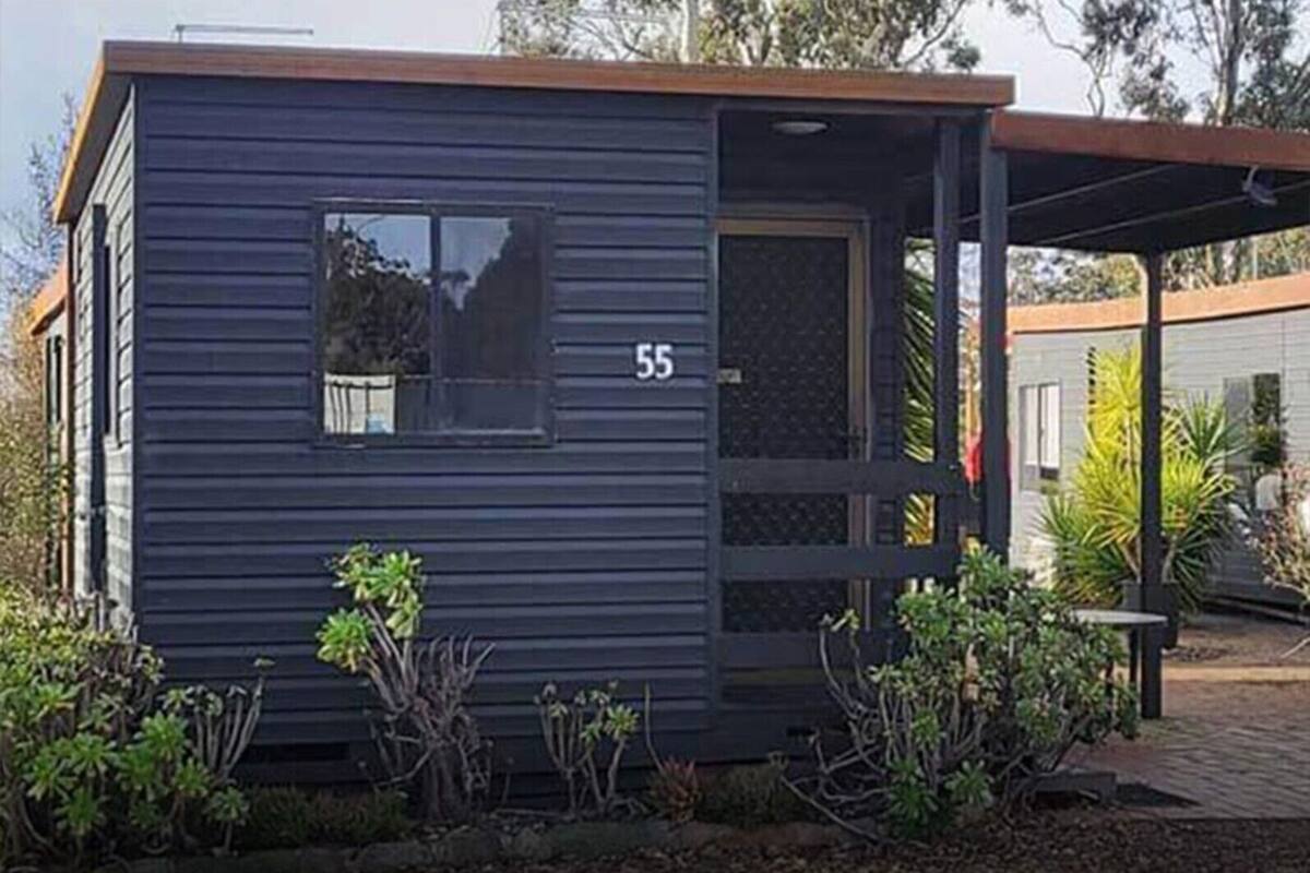 Un edificio pequeño y de color oscuro con el número '55' en el lateral, una ventana y una puerta.
