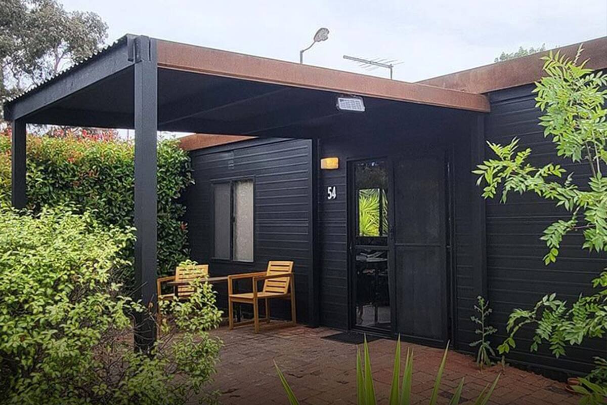 Un edificio negro con un patio cubierto, un letrero con el número 54 y una puerta con ventana.