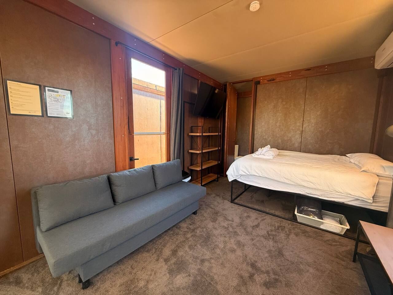 Une pièce de taille modeste, comprenant un canapé, un lit, un téléviseur et une étagère en bois.