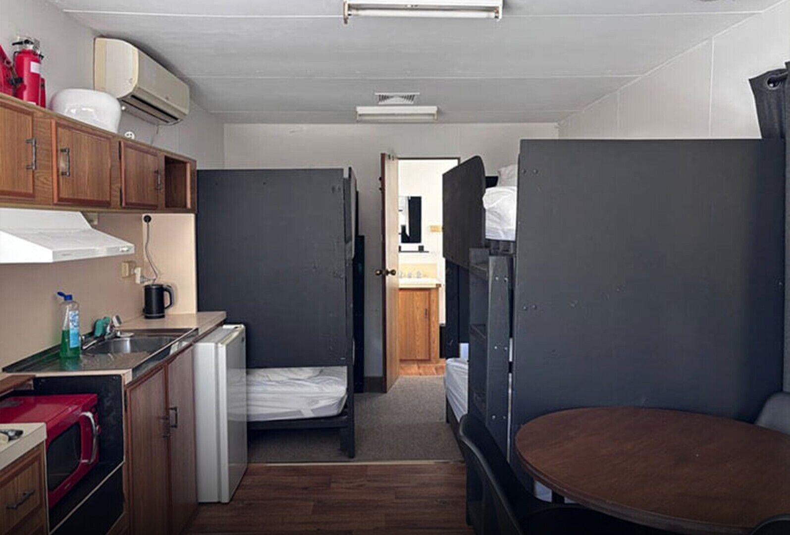 A compact room with a kitchenette, a bed, a small table, and a door leading to another room.