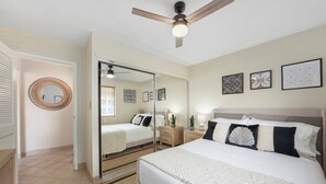Ein Schlafzimmer mit einem großen Bett, einem Deckenventilator, einem Spiegel und gerahmten Kunstwerken an der Wand.