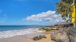 Ein Strand mit blauem Himmel, ruhiger Wellen und großen Felsen.